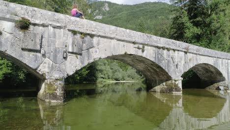 drone fly through of an old beautiful bridge in the mountain with a woman