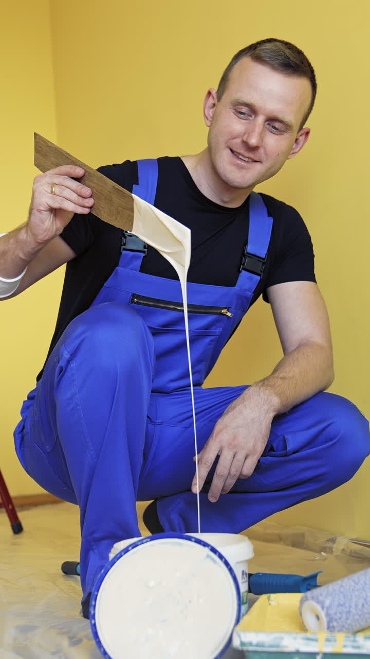 Repair and decorating walls in the house. Worker in blue overalls prepares color before painting walls in the room. Builder man working indoors. Makeover at home. Vertical video