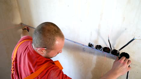 electricista comprobando los parámetros técnicos con cinta métrica y herramienta láser de haz rojo en el sitio de construcción