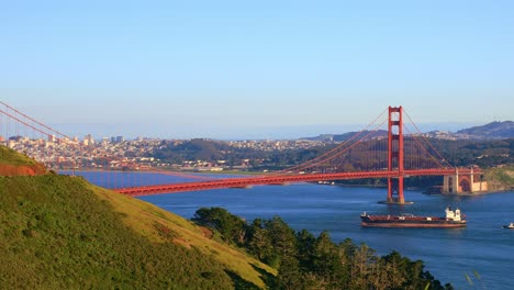 the golden gate bridge from a scenic view point looking over the bay with a cargo ship passing under during sunset with warm light and blue skies