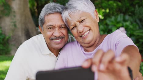 Video-of-happy-biracial-senior-couple-taking-selfie-in-garden