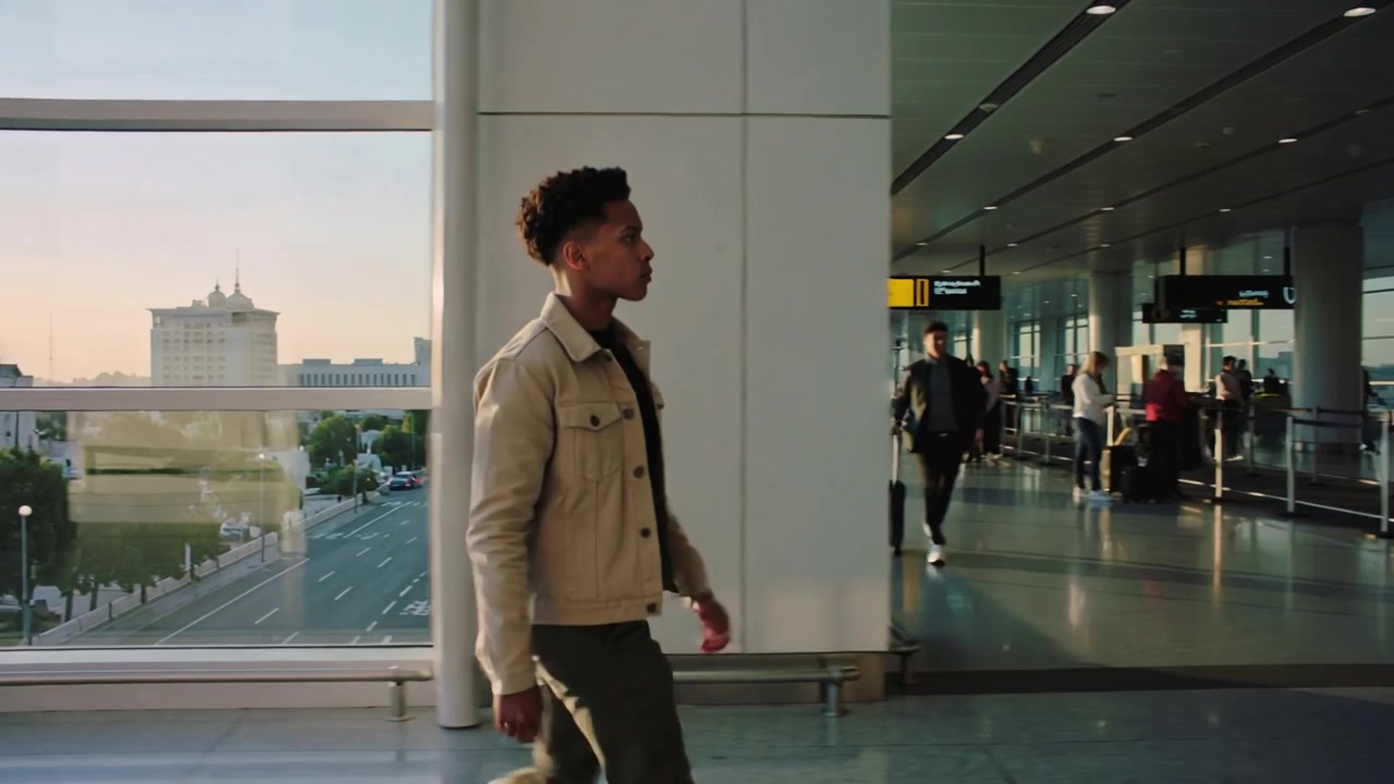 Homme marchant portant une veste beige clair, s'éloignant de la fenêtre et scannant la signalisation du terminal pour trouver la porte d'embarquement