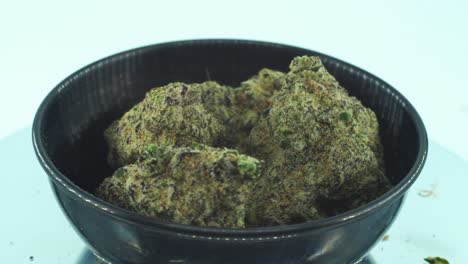 close up shot of a marijuana sativa super lemon amnesia haze rock flowers, yellow, green and purple kush, on a reflecting 360 rotating stand, in a black shiny bowl, slow motion 4k video