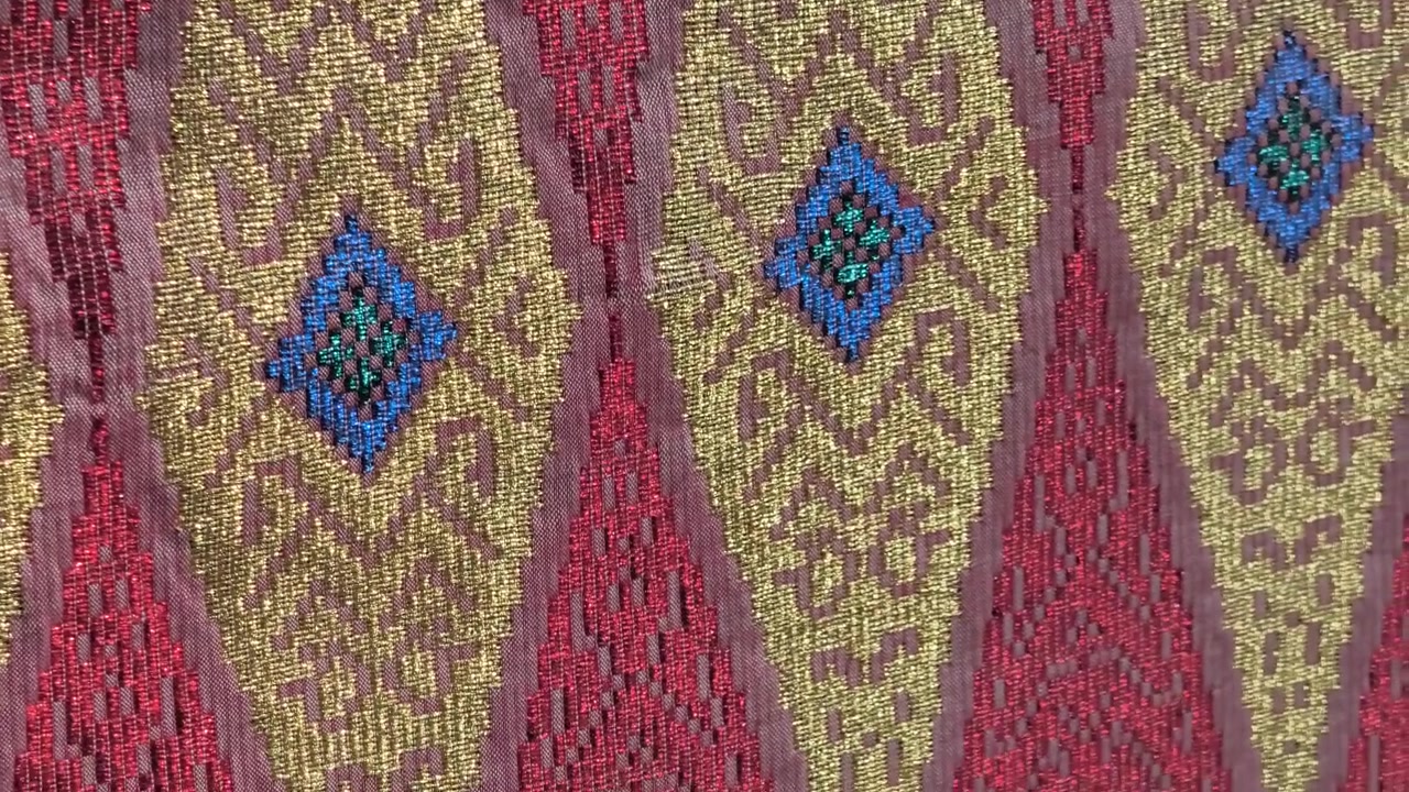 Detailed close-up of luxurious Songket fabric. The intricate gold embroidery shines across the handwoven surface. This prestigious Malaysian textile is reserved for the most special occasions.