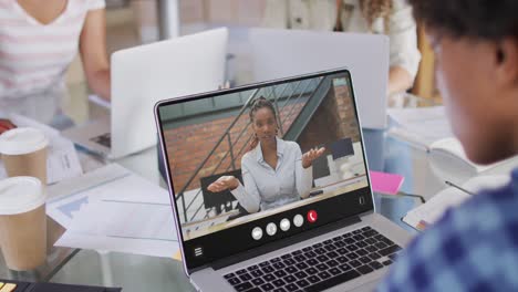 hombre afroamericano usando una computadora portátil para una llamada de video, con un colega de negocios en la pantalla