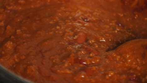 stirring delicious red chili in pot with wood spoon macro