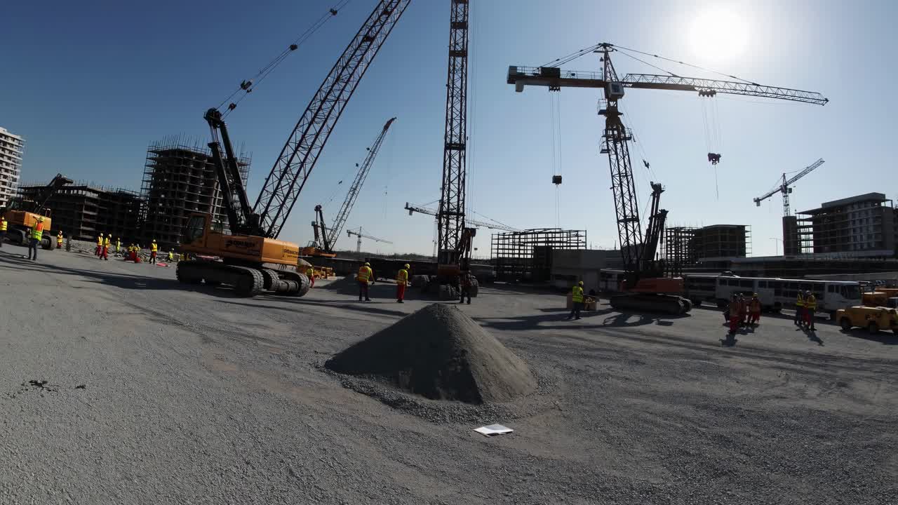 Wide-angle video shot of a bustling construction site with cranes and workers under a clear blue