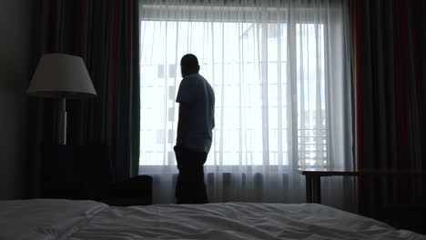 불안한 중년 남자가 어두운 호텔 방을 가로질러 걸어가는 중간  ⁇