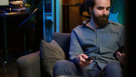 happy man holding remote control chatting on smartphone