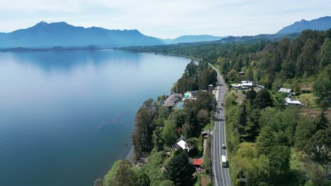 aerial view of serene lake and winding road surrounded by lush forest and distant mountains on a clear day