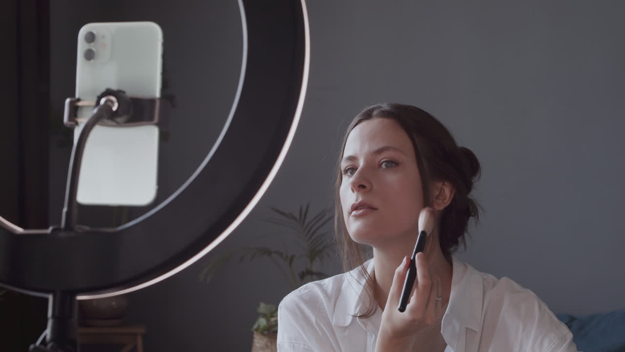 симпатичная девушка-блогер снимает видеоурок по нанесению пудры для макияжа кистью на лицо