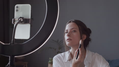 pretty vlogger girl makes a video tutorial applying make up powders with a brush on her face