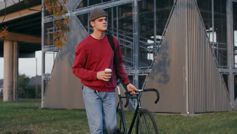 hombre caminando con una bicicleta fija y café en un parque de la ciudad