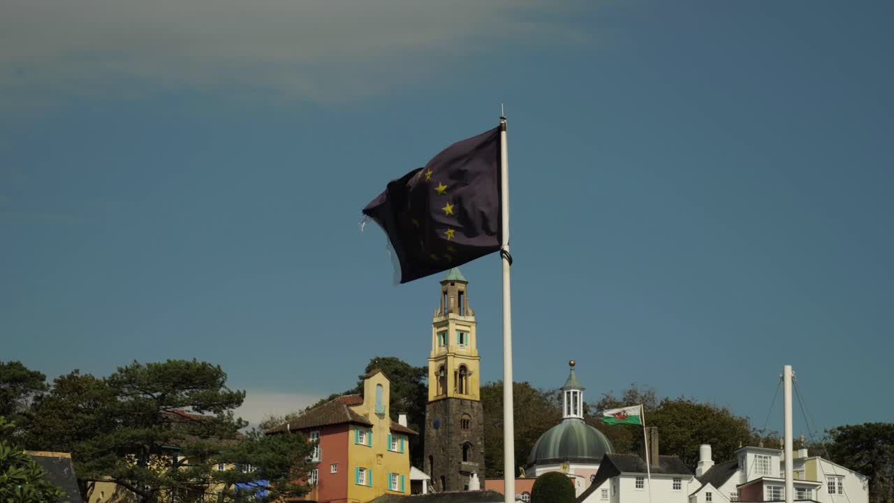 Bandiera dell'Unione Europea che sventola in primo piano, bandiera gallese con il villaggio di Portmeirion sullo sfondo
