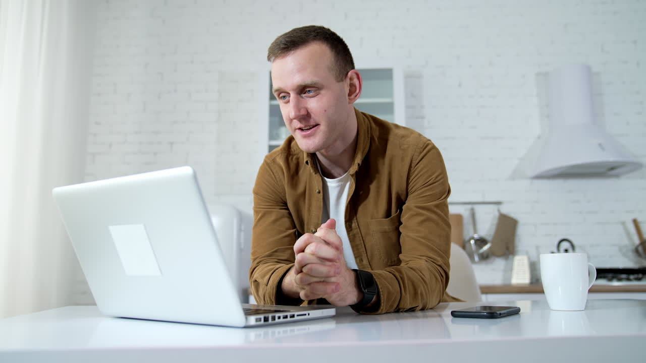 Young man giving a consultation online. Male freelancer having a video call on a laptop in the kitchen. Remote job. Distance education.