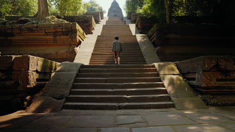 person walking up grand stone stairs towards an ancient temple