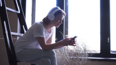 charming girl using phone while sitting near window