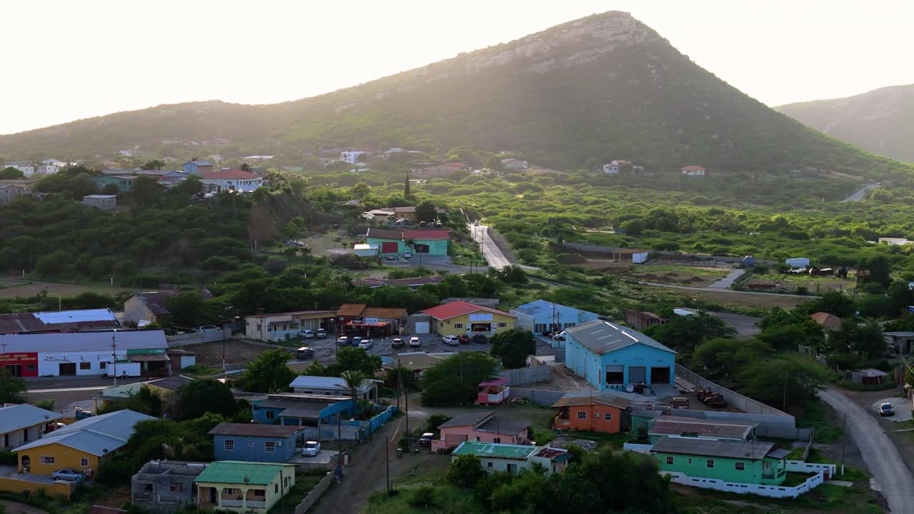 Vibrant colorful Caribbean homes in Curacao under shadow of cloud as golden light falls on beautiful tropical hills