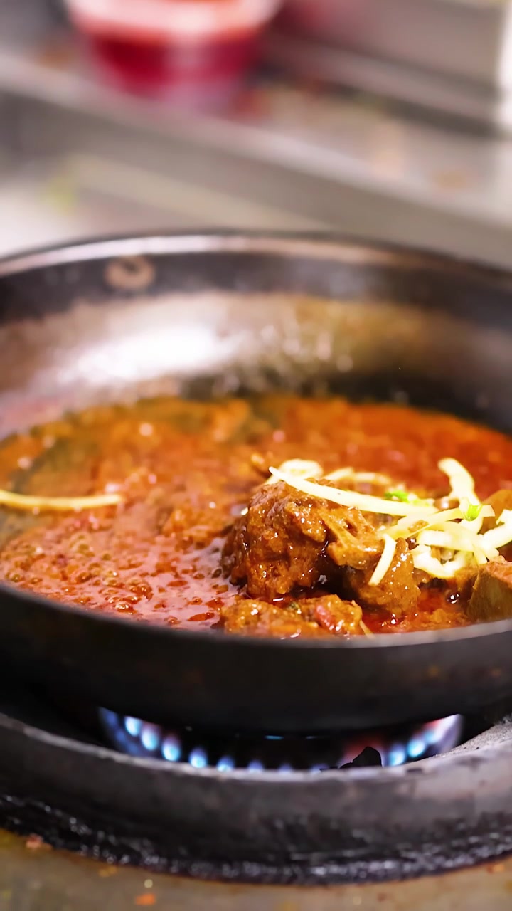 Close-up kari daging pedas yang mendidih perlahan di wajan di atas api gas biru.