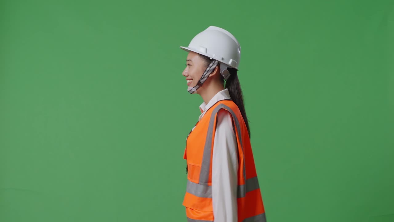 안전 헬을 착용하고 녹색 스크린 배경 스튜디오에서 고 있는 아시아 여성 엔지니어의 측면 시각