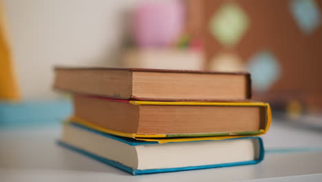 Little-girl-hands-put-pile-of-books-on-desk-in-classroom