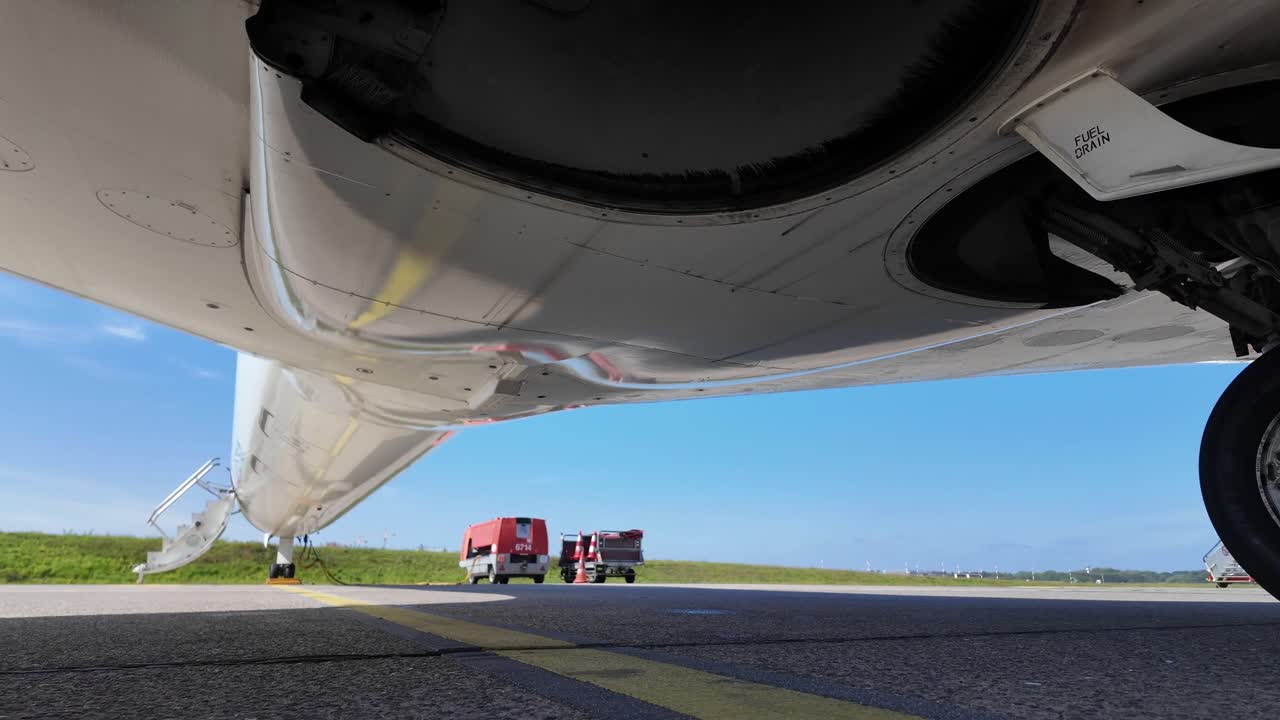 External view, extreme low angle, of the lower part of the fuselage and wheels of a white color fuselage jet parked on the ramp in a bright sunny day