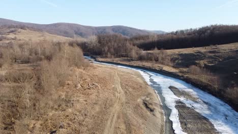 Drone-shot-of-the-forest-and-a-country-icy-river-in-the-late-autumn