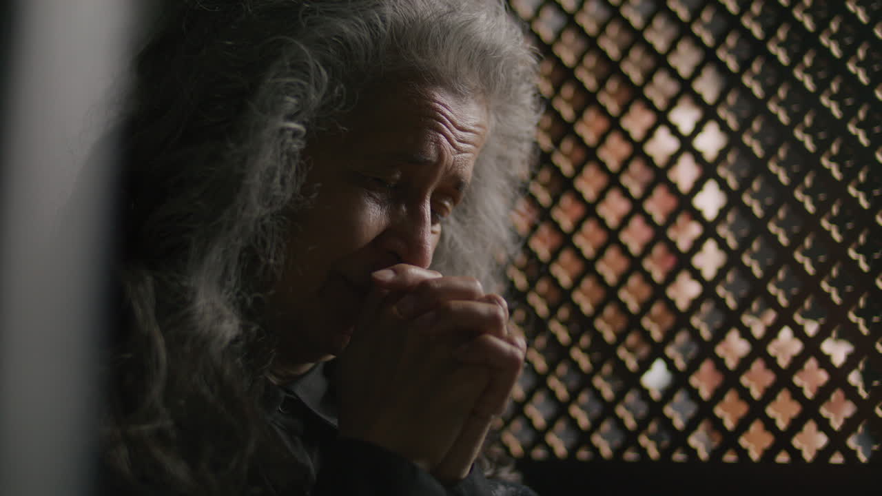 Sorrowful Elderly Woman Praying beside Lattice Screen during Confession