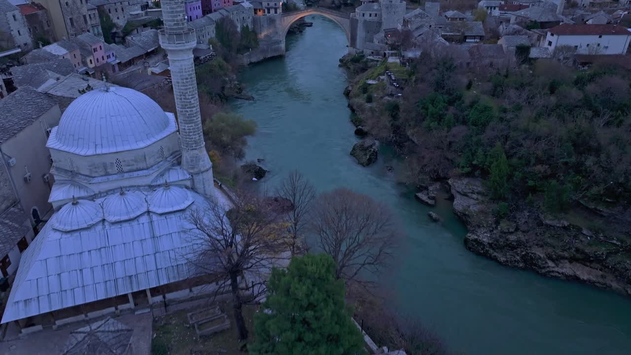 Huzurlu nehir kenarlarının üzerinde parlayan tarihi köprünün drone görüntüsü.