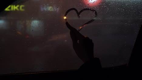 the glass of the window is swamped. young girl with forefinger draws a symbol of love and heart. st. valentine's day