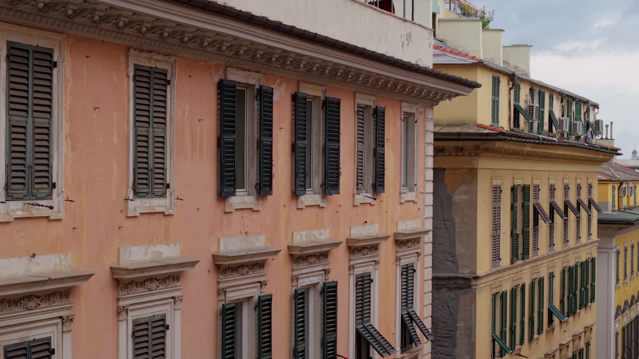 Drone moves laterally between old Genoa buildings showing windows, shutters, and facades