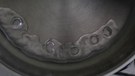 slow-motion view capturing the moment water splashes into a hot stainless steel pan, connecting in a semi-circular motion