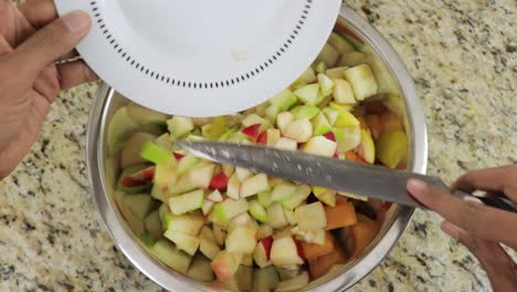 hands adding chopped fruits in a bowl