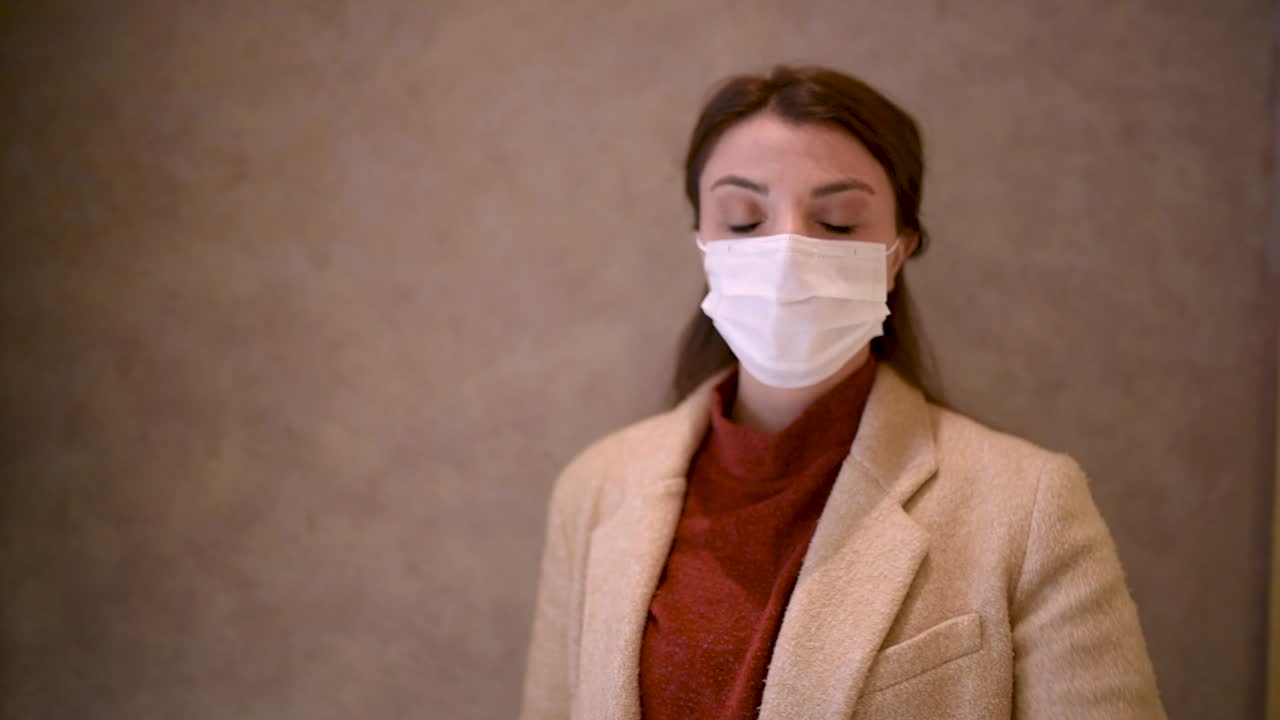 보호용 의료용 마스크와 유행하는 옷을 입은 아름다운 소녀가 정지 신호로 손을 들고 있습니다.