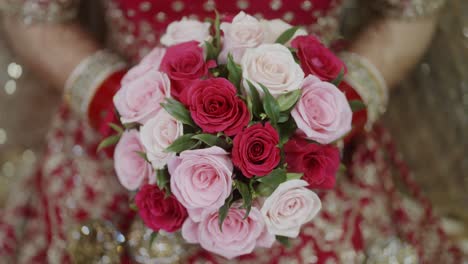 indian bride holding bouquet of red and pink roses in hand on wedding day