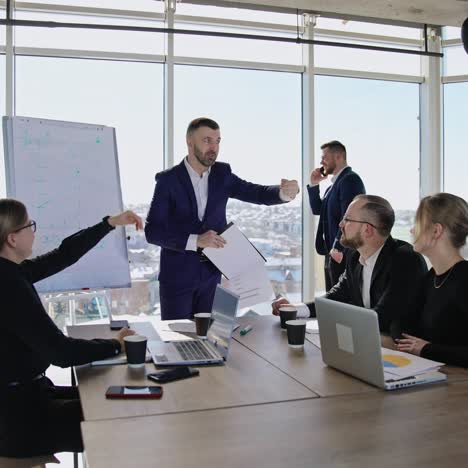 colleagues sitting at the table in front of laptops and listening to the speaker. male partner standing at the window and speaking on the phone at the backdrop