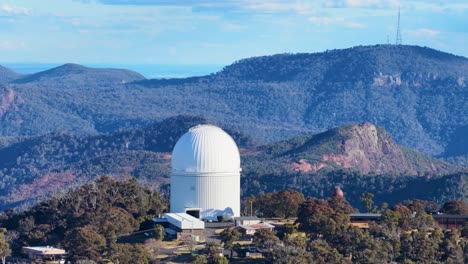 aerial footage shows a white observatory dome amid forested hills and mountains, with smooth lateral camera movement and warm, natural sunset lighting