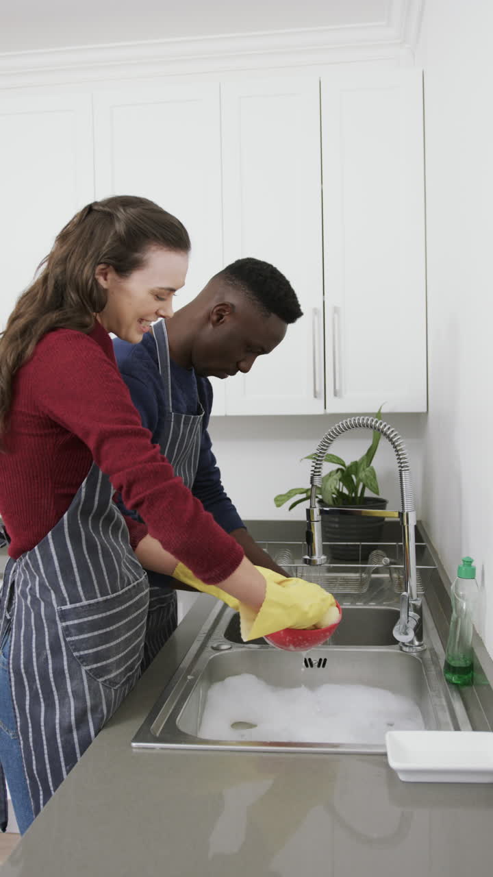 Coppia felice e diversificata che sorride e lava i piatti in cucina, al rallentatore, con spazio per il testo