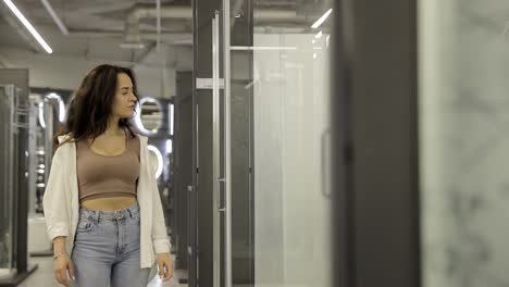 beautiful smiling woman looking for shower cabin in bathroom furniture store beautiful smiling woman looking for shower cabin in bathroom furniture store a woman in a store chooses a shower cabin for her new home concept of repair arrangement