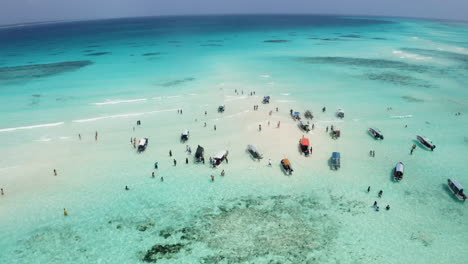 People-walking-in-shallow-tropical-ocean-waters-between-anchored-boats