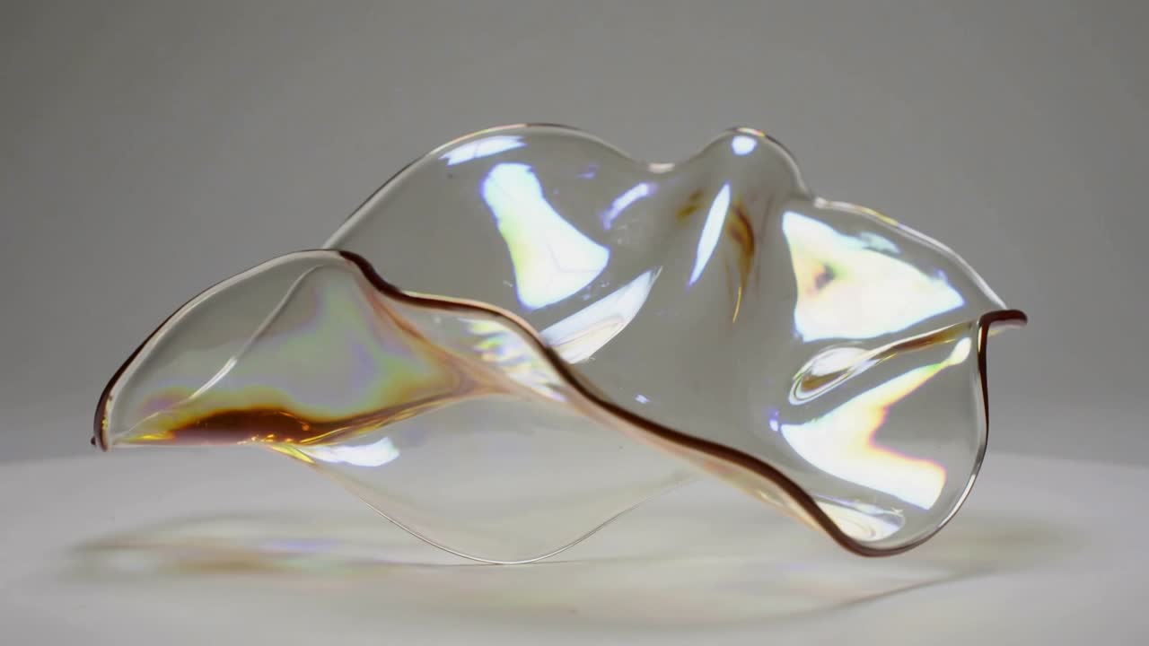 Iridescent sheet rotating, morphing above table, frames driving rotation, showing glints for design