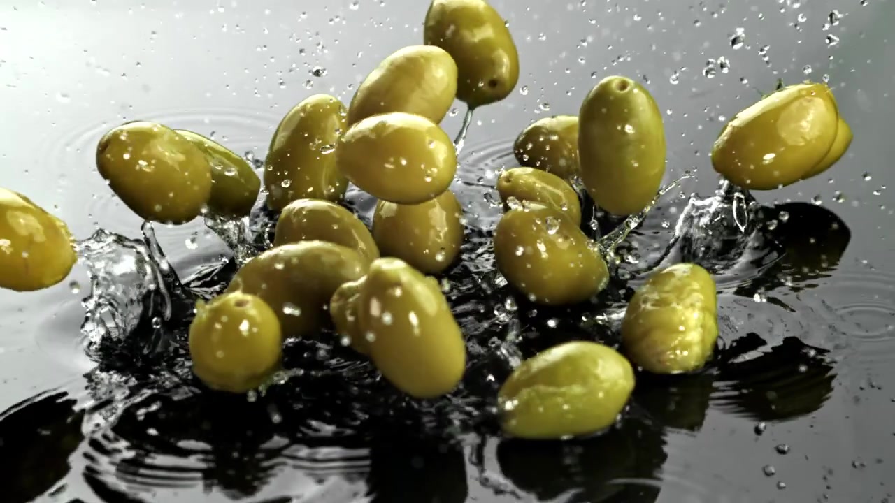 Olive verdi che cadono e schizzano nell'acqua al rallentatore.