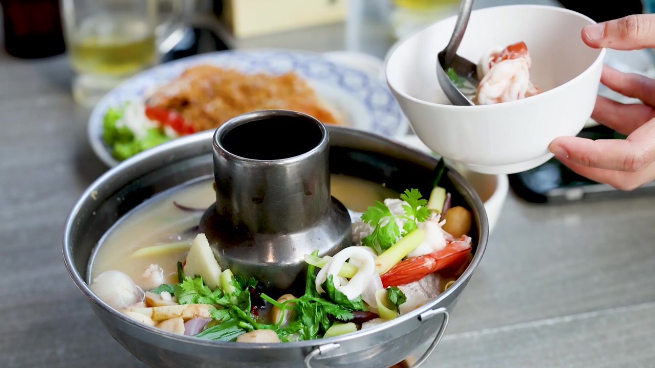 Một người múc món súp hải sản cay từ nồi lẩu kim loại truyền thống vào bát
