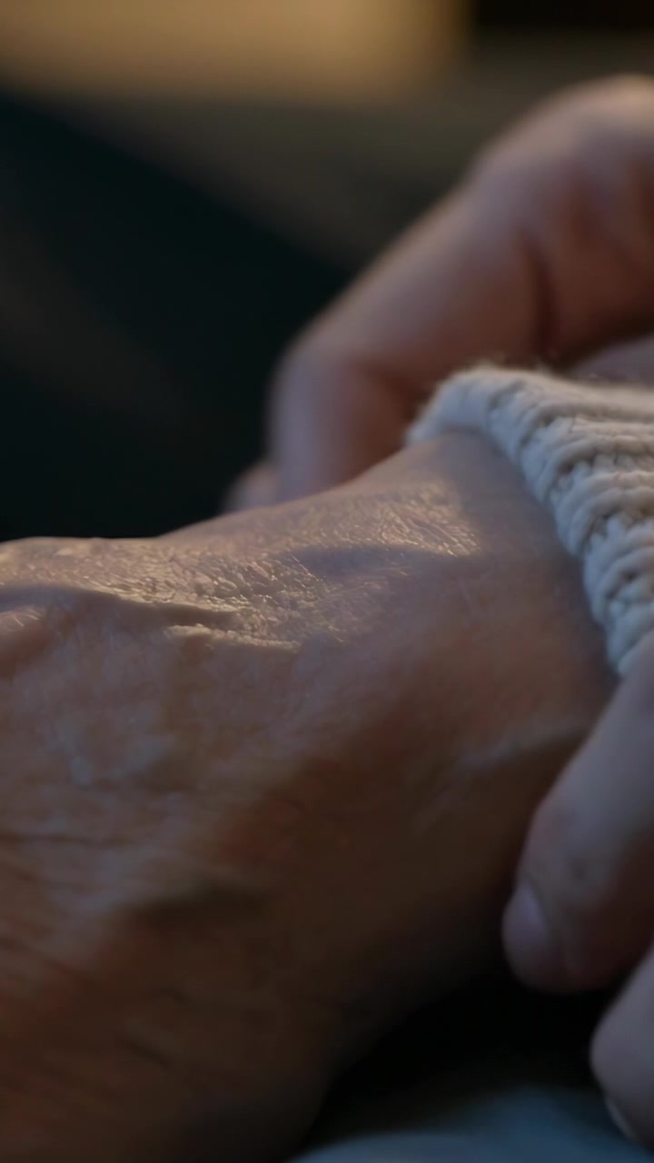 Video verticale: Una mano che entra e posiziona un polsino color crema sul polso di un anziano sul letto per calore.