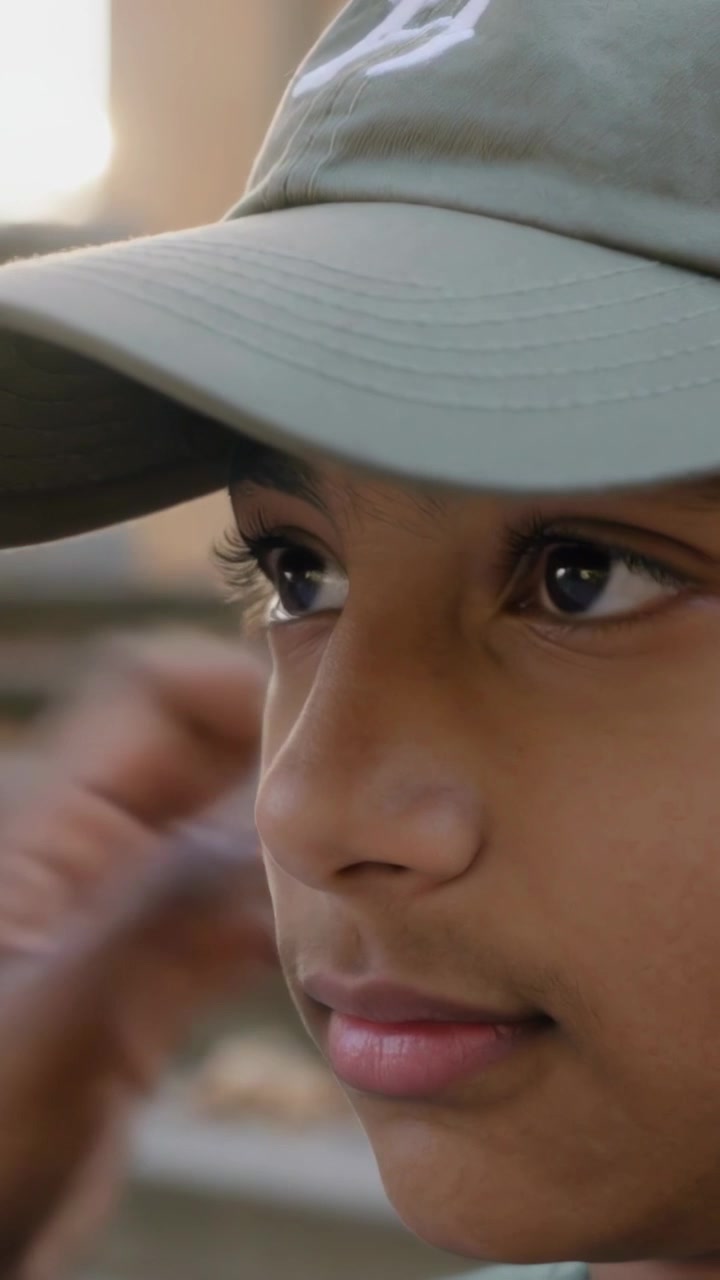 Vertical video: Lifting hands teen in grey hoodie adjusting olive cap brim to shade eyes on steps