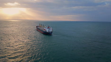 bulk carrier ship sailing to sunset. drone view vessel floating in dark ocean.