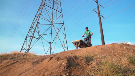 man on mountain bike launches over a wood ramp on top of a hill