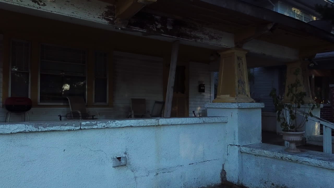 съемка с беспилотника с воздуха в обратном направлении над белым заброшенным ветшающим домом с разбитыми окнами и припаркованной перед ним полицейской машиной