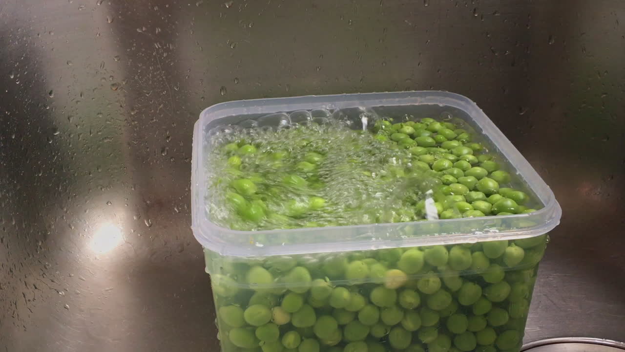 imágenes de mujer lavando y enjuagando guisantes verdes con colador de inox en un fregadero a cámara lenta