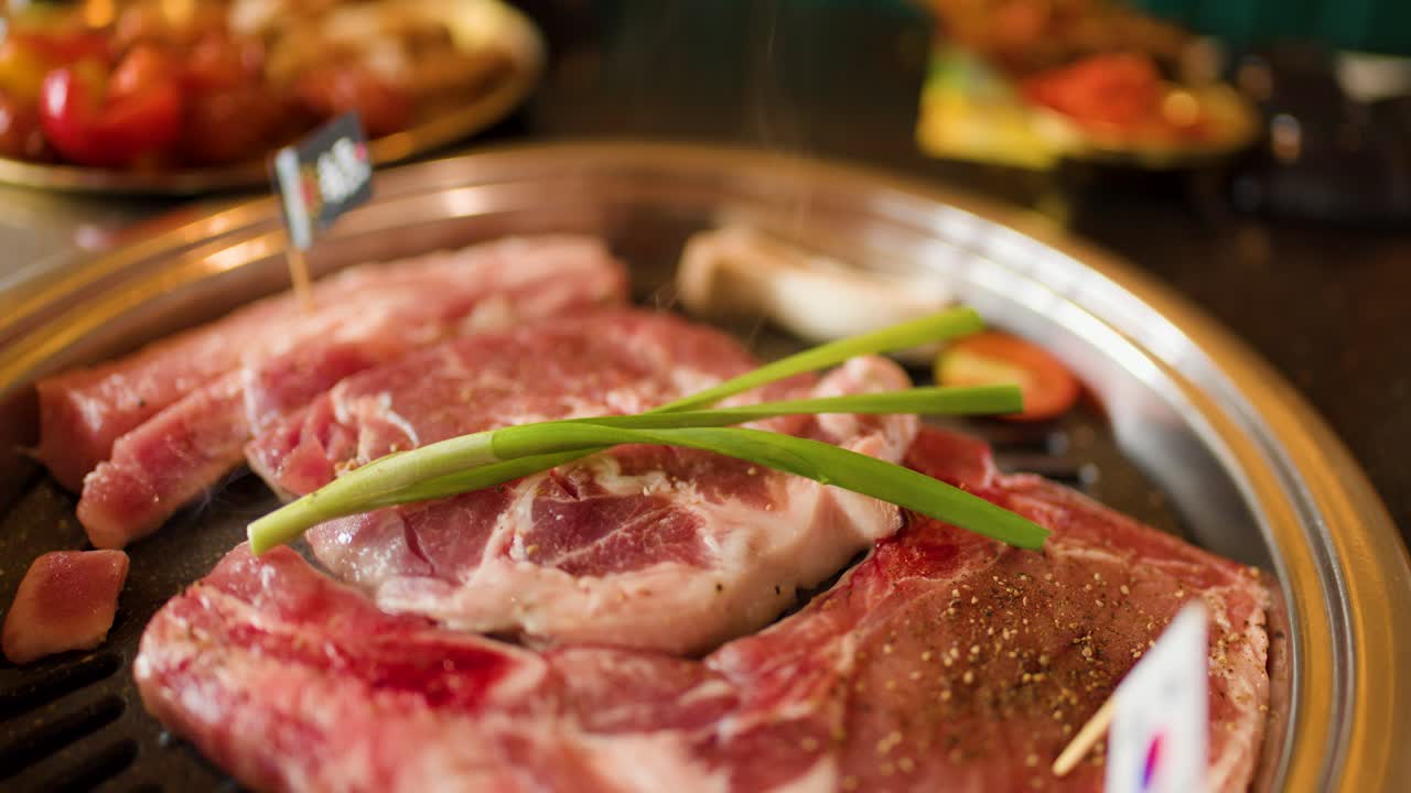 Close-up of raw beef and vegetables on grill pan, steam rising, shallow depth of field